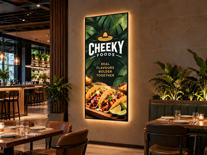 Single panel backlit restaurant sign for Cheeky Foods on a beige wall, with a dark tropical leaf background and two tacos with lime wedges. Brands and artwork shown are for illustrative purposes only.